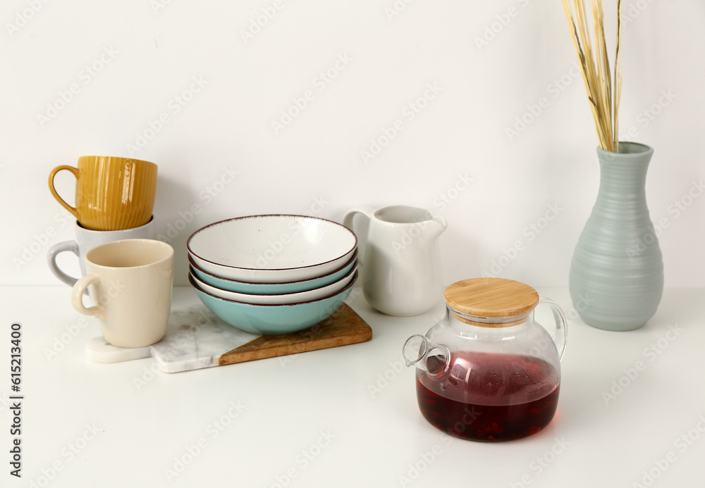 Composition with glass teapot and different kitchen utensils on white table