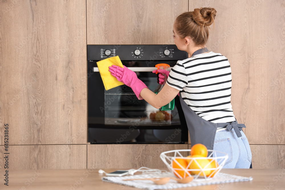 Pretty young woman in pink rubber gloves cleaning electric oven with sponge and detergent