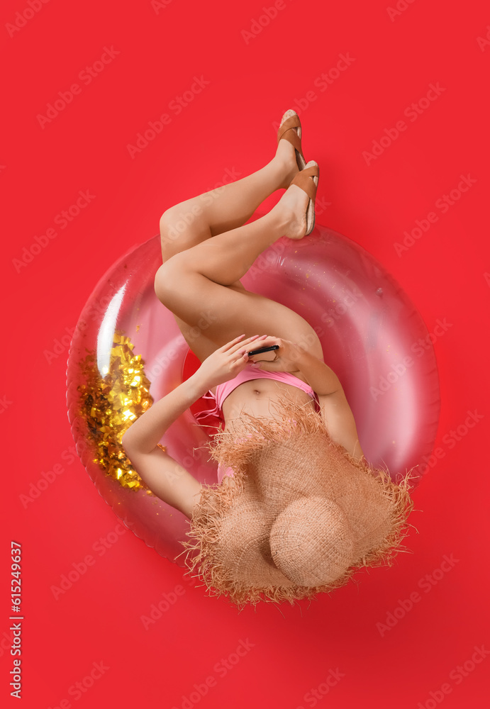 Young woman in swimsuit with inflatable ring using mobile phone on red background, top view