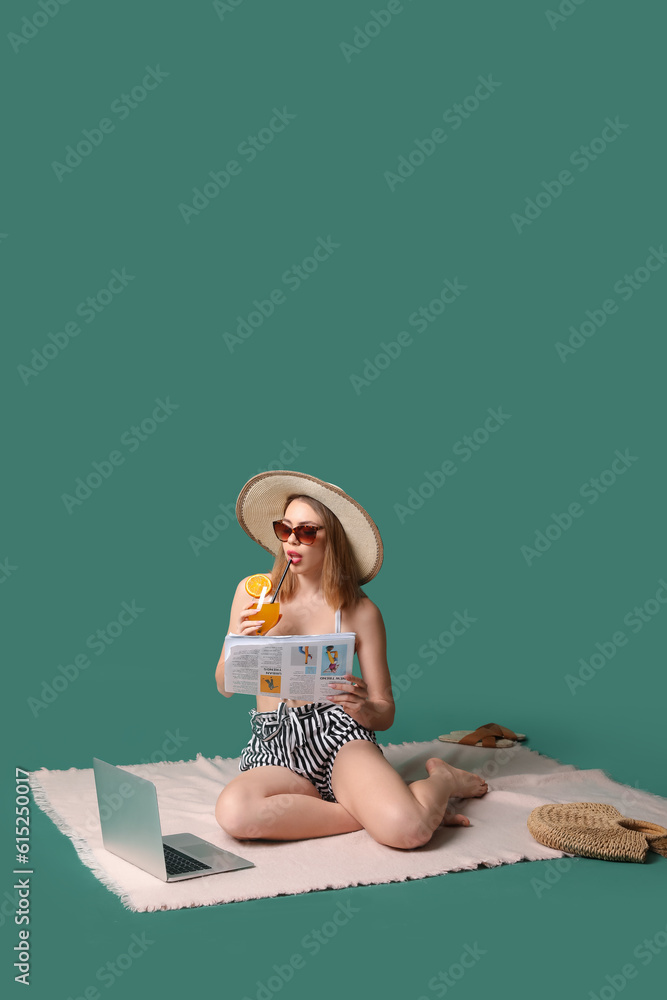 Young woman with cocktail and beach accessories on green background