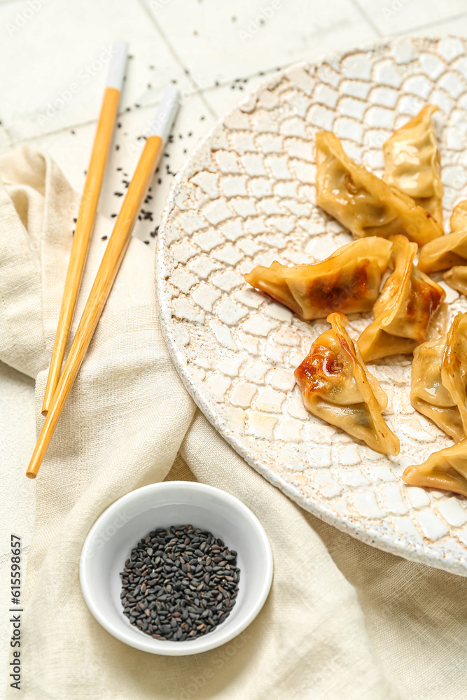 Plate with tasty Chinese jiaozi and sesame on white tile background