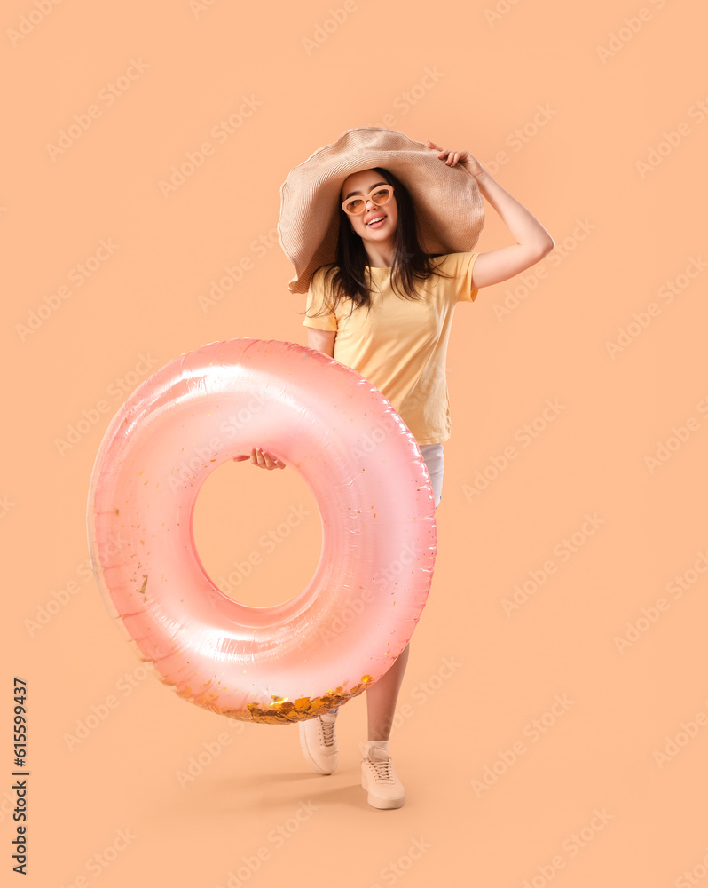 Young woman with pink inflatable ring on beige background