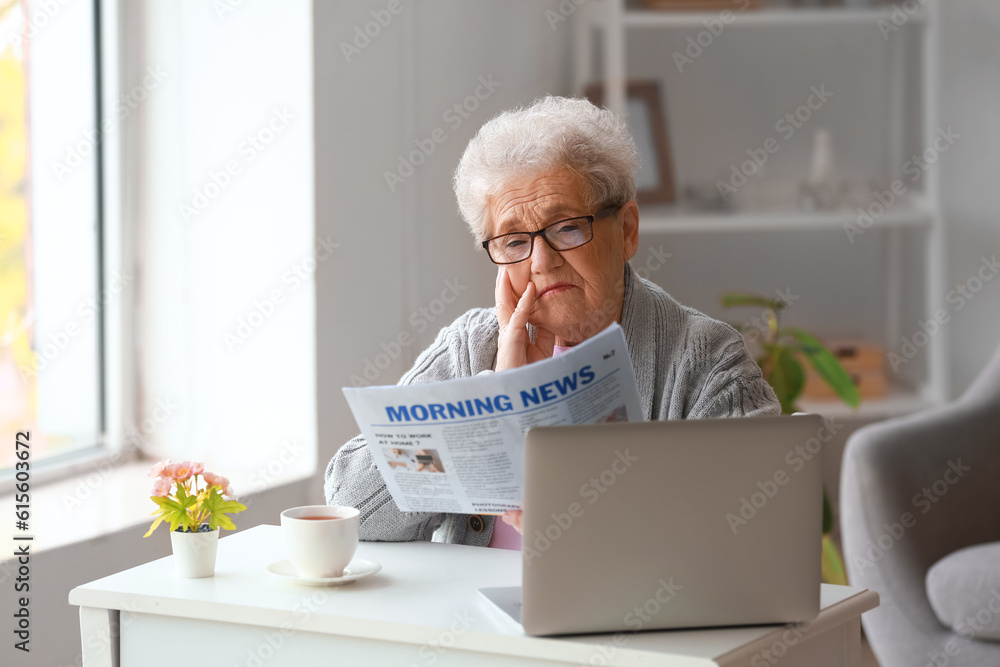 Senior woman reading newspaper at home