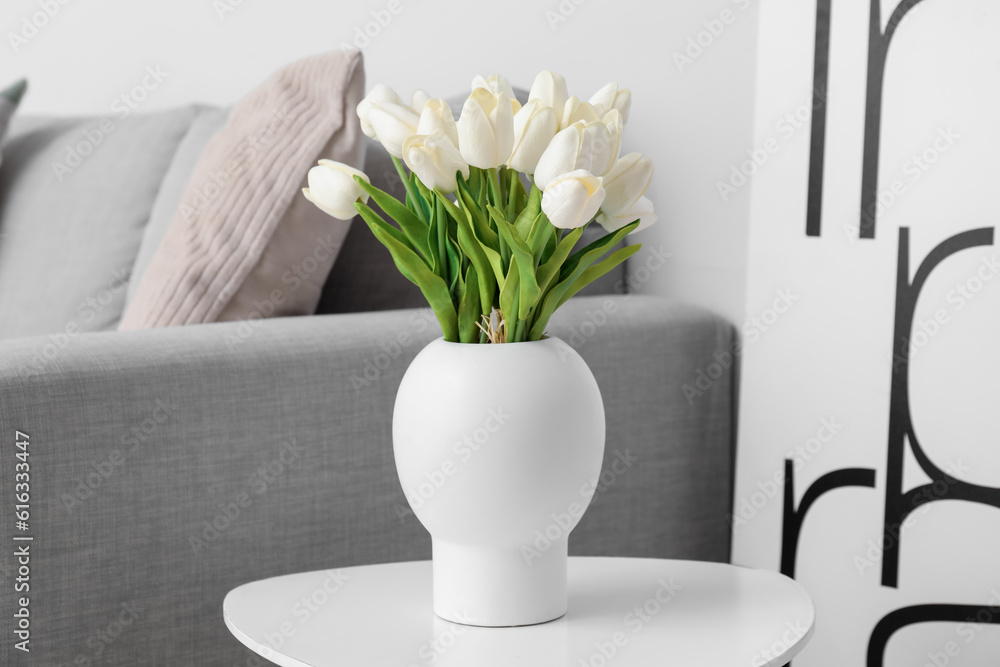 Vase with beautiful tulip flowers on table  near grey sofa
