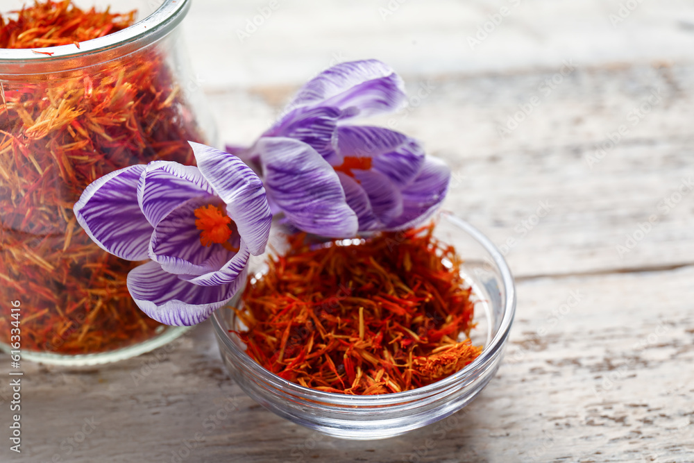 Jar and bowl of dried saffron threads with crocus flowers on white wooden table
