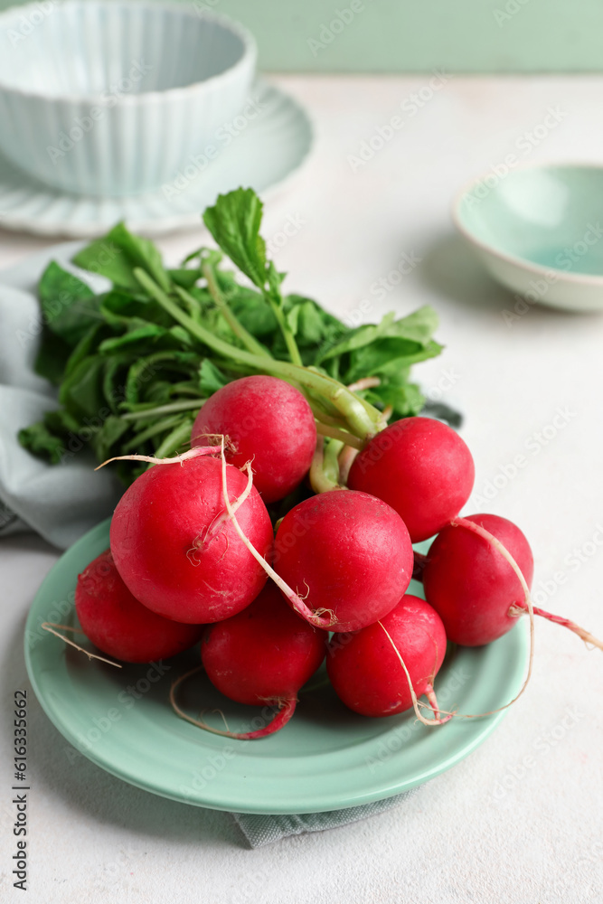 Bowls and plate of fresh radishes with leaves on light background