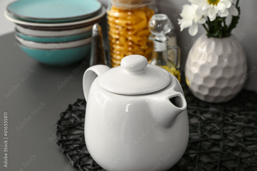 Teapot with flowers and different kitchen stuff on black table