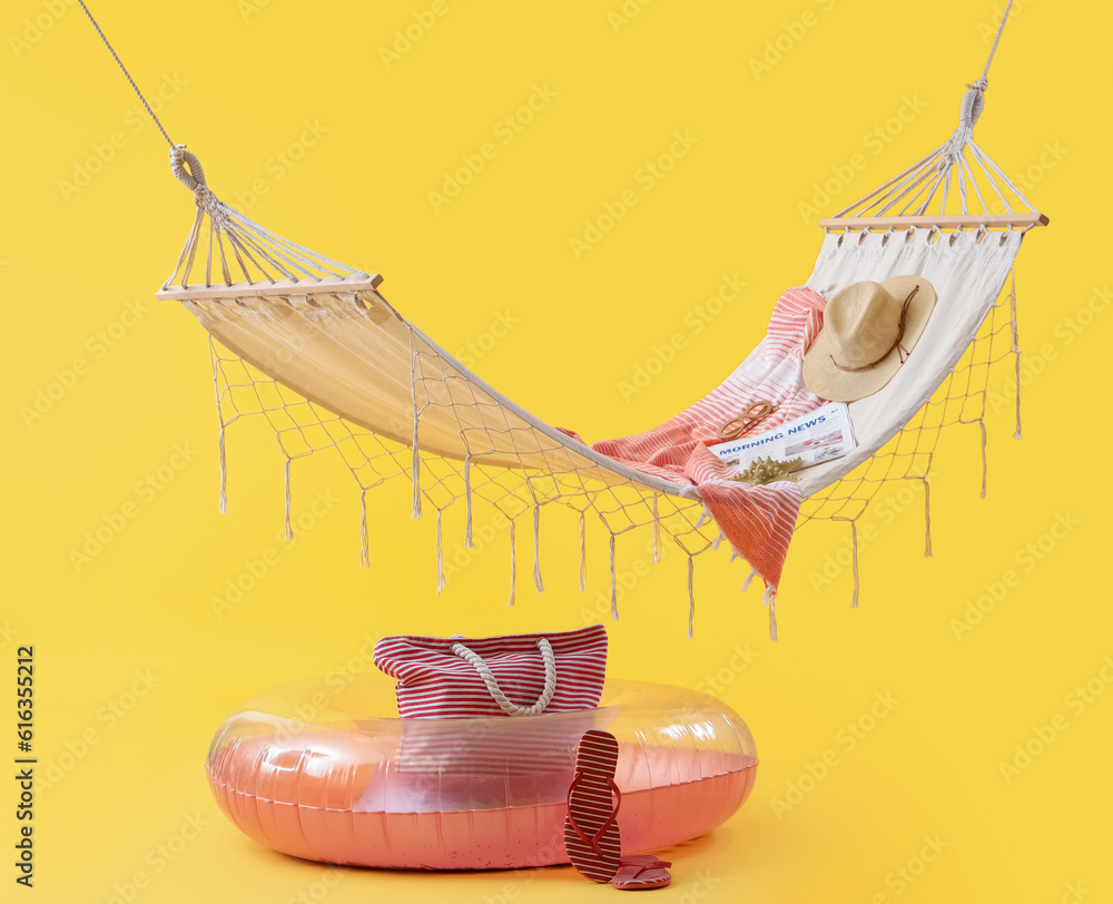 Cozy hammock with inflatable ring and different beach accessories on yellow background. Summer vacat