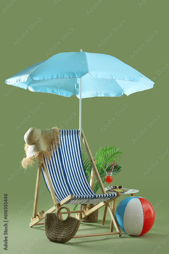 Composition with deckchair, umbrella, beach accessories and cocktail on stool against green backgrou