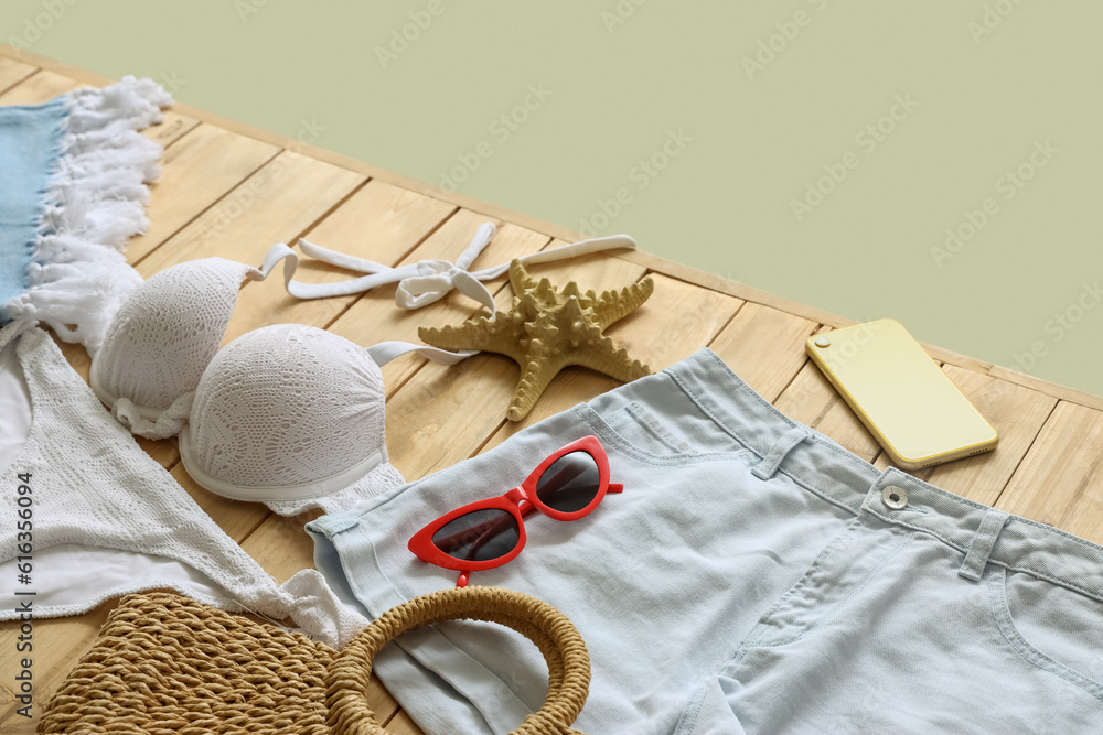 Clothes with beach accessories, starfish and mobile phone on wooden pontoon against green background