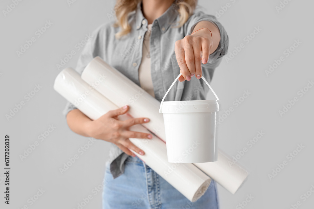 Young woman with wallpaper rolls and glue on grey background, closeup
