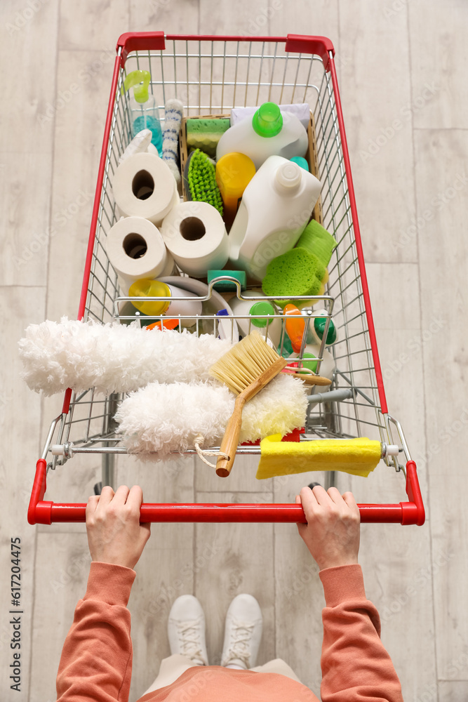 Woman with shopping cart full of cleaning supplies on wooden floor, top view