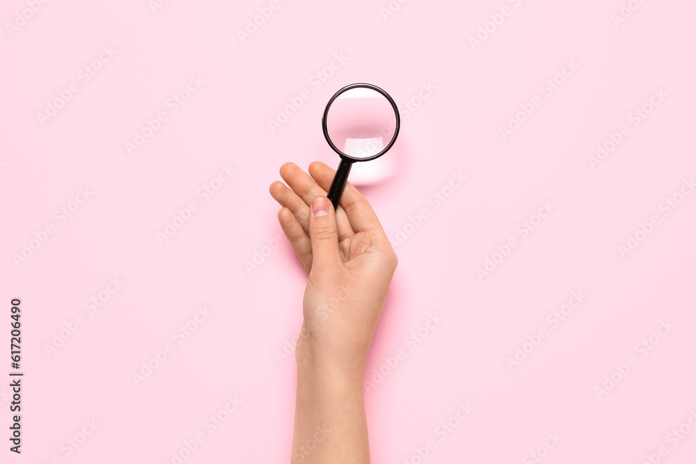 Female hand with magnifier on pink background