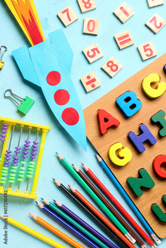 Color paper rocket with abacus, wooden letters and pencils on color background