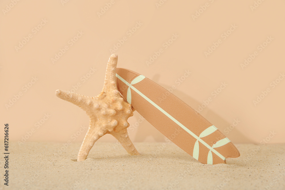 Mini surfboard with starfish on sand against beige background