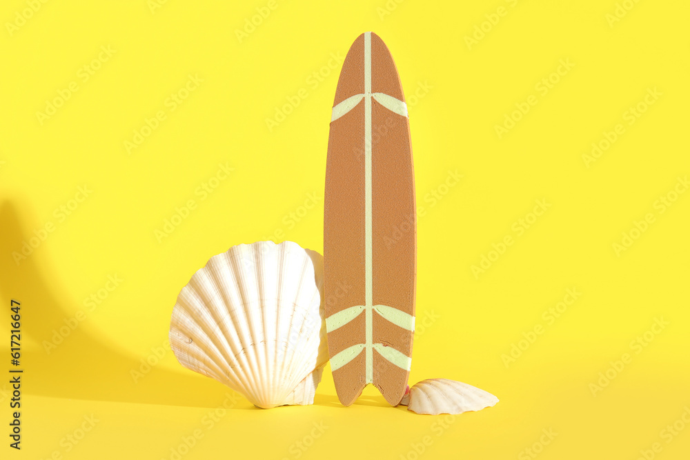 Mini surfboard with seashells on yellow background