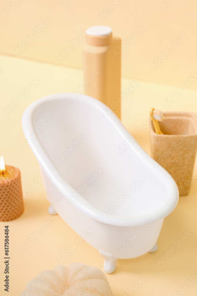 Small bathtub, burning candle and bath supplies on color background