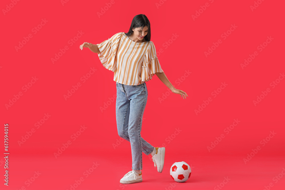 Young woman playing with soccer ball on red background