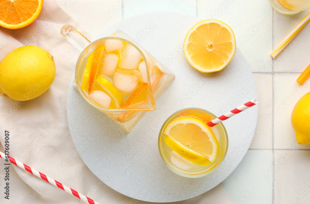 Jug and glass of infused water with lemon on white tile background