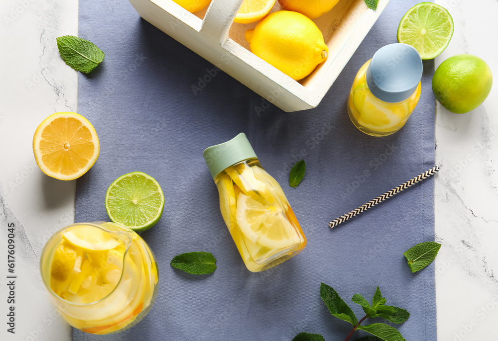 Bottles and jug of infused water with lemon on white marble background