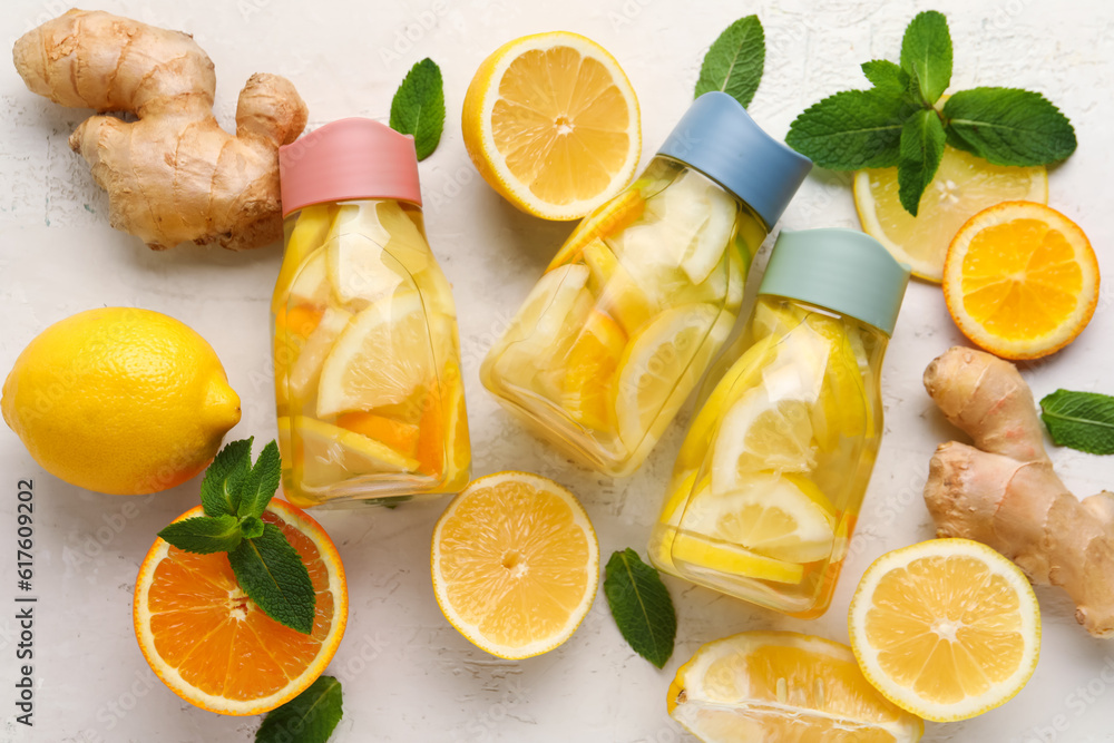Bottles of infused water with lemon and ginger on light background