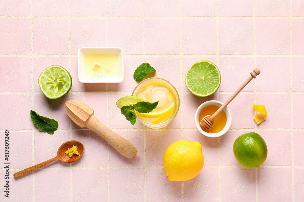 Glass of infused water with citrus fruits, juicer and honey on pink tile background