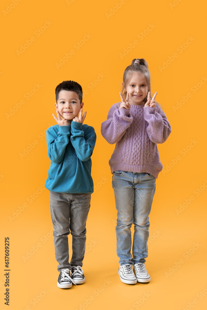 Cute little children in knitted sweaters showing victory gesture on yellow background