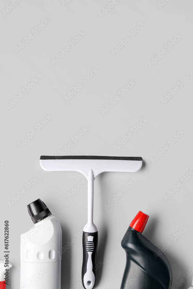 White plastic squeegee and bottles of detergent on grey background