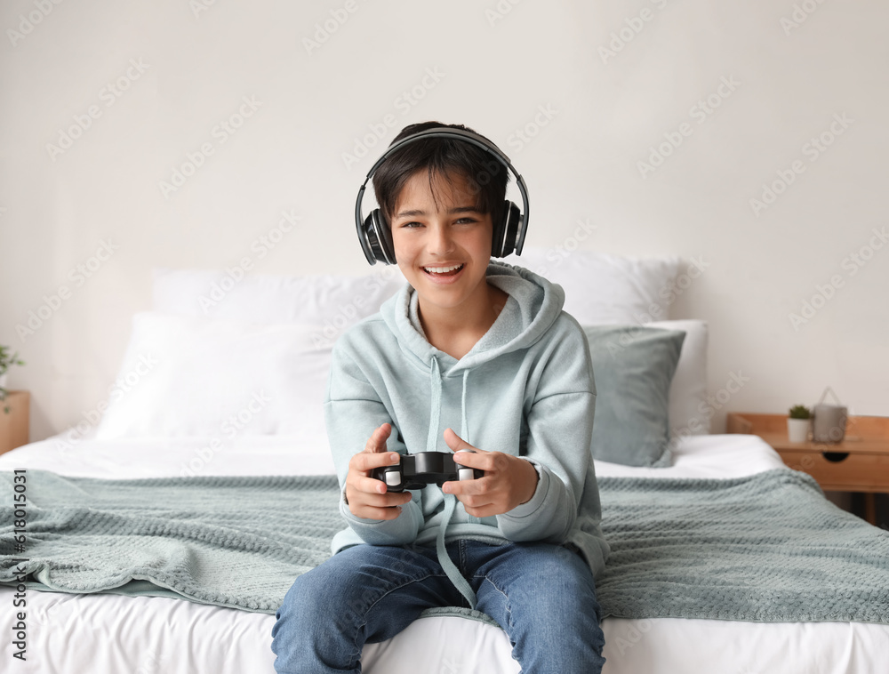 Little boy with headphones playing video game in bedroom