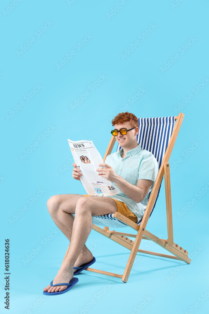 Young man reading newspaper in deck chair on blue background