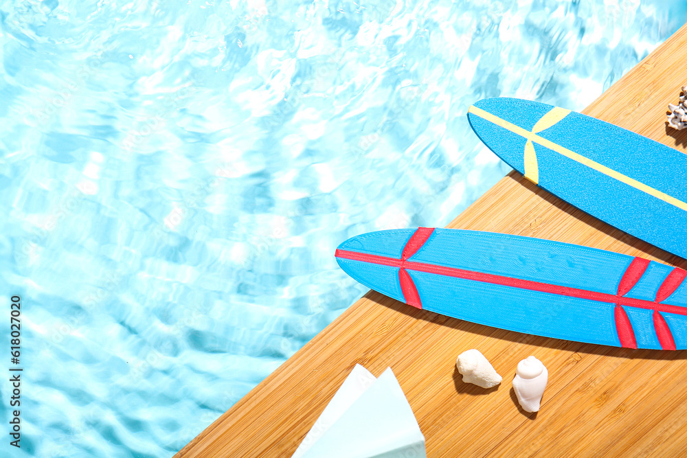 Composition with mini surfboards, umbrella and seashells on edge of swimming pool