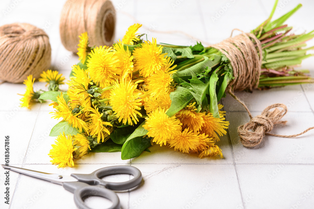 Bouquet of beautiful dandelion flowers, rope and scissors on light tile background, closeup