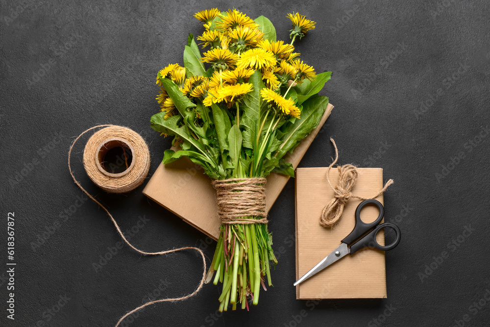 Bouquet of beautiful dandelion flowers, rope, scissors and books on dark background