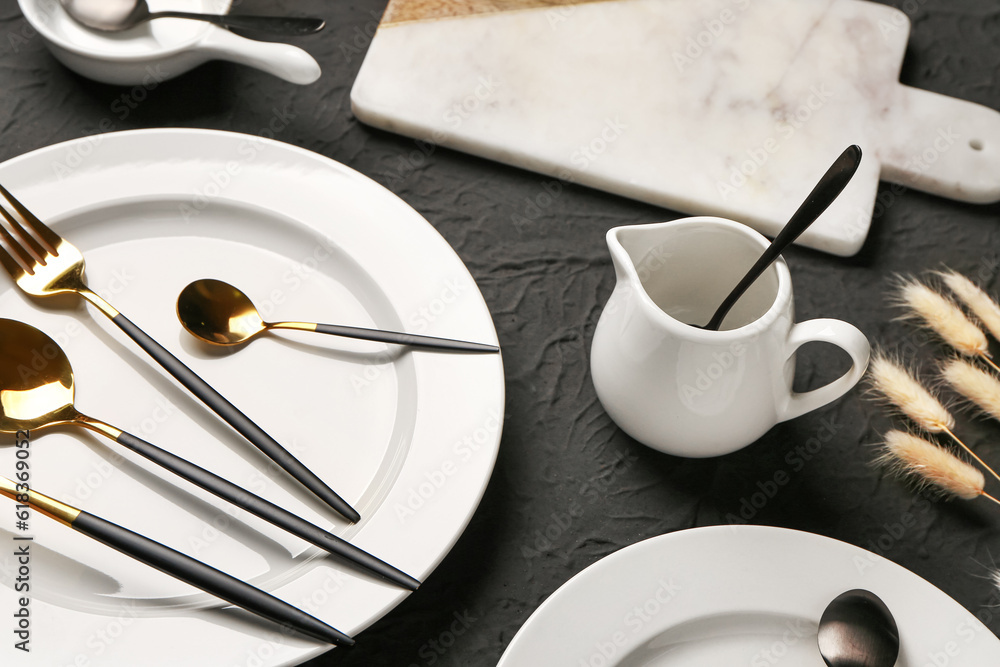 Table setting with clean plates, cutlery and pitcher on black background