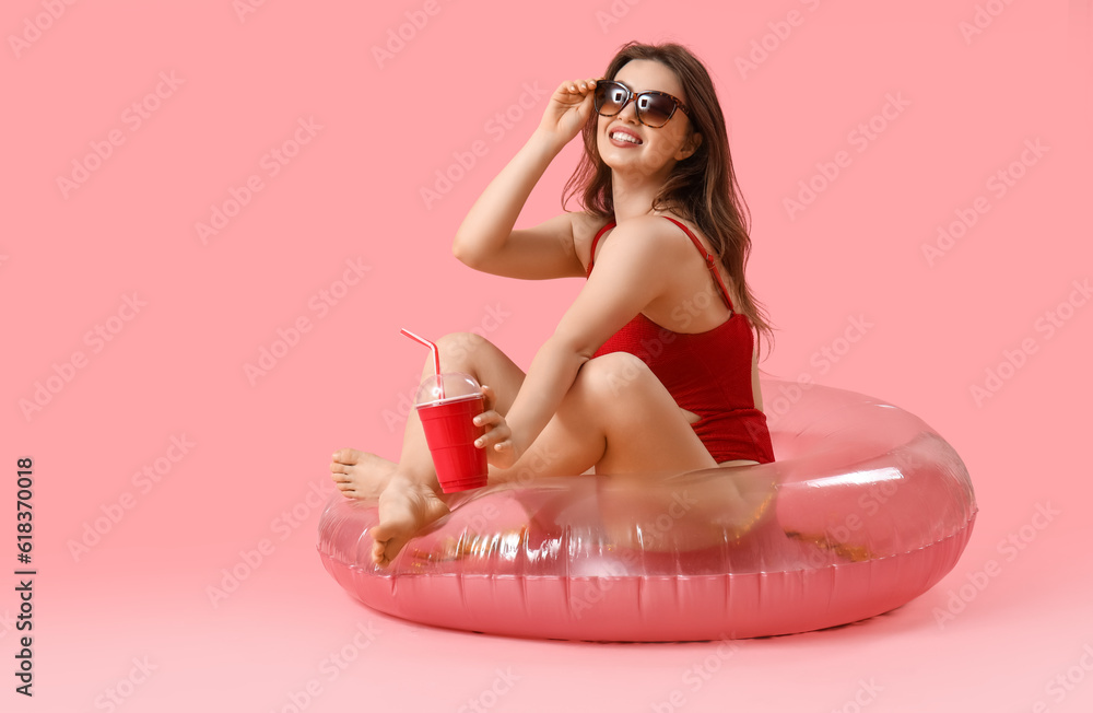 Young woman with soda and swim ring on pink background