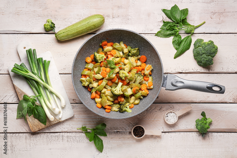 Frying pan with different vegetables on light wooden background