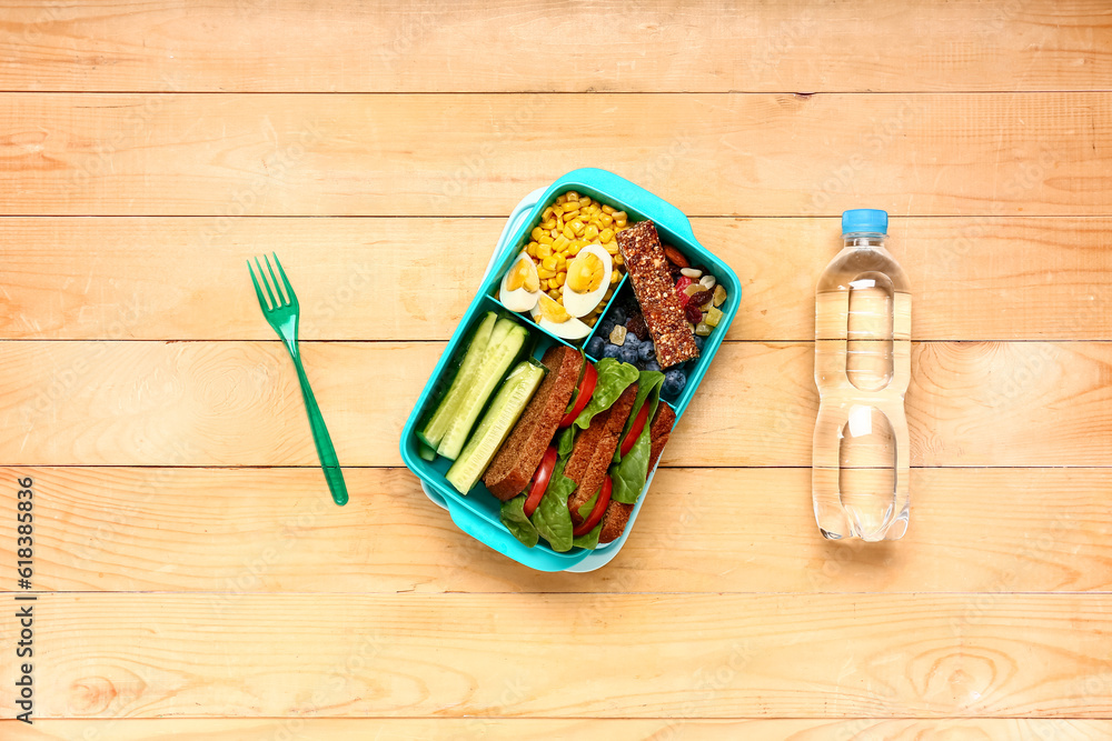 Bottle of water, fork and lunchbox with tasty food on brown wooden background