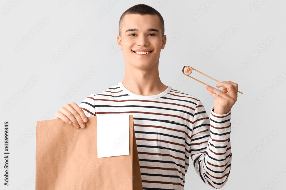 Young man with tasty sushi and paper bag on light background