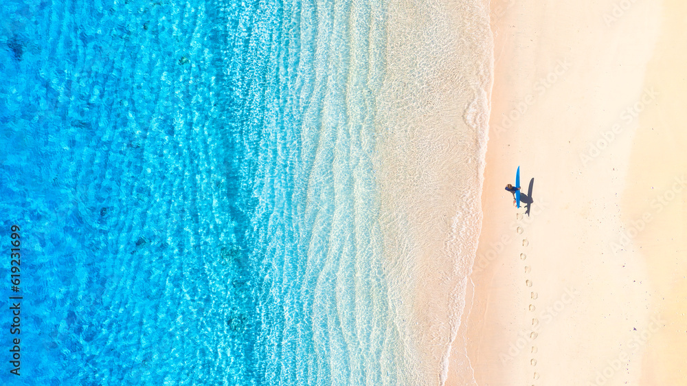 Surfer with a board on the beach. Blue water and clean beach in the summer. View from a drone. An ae