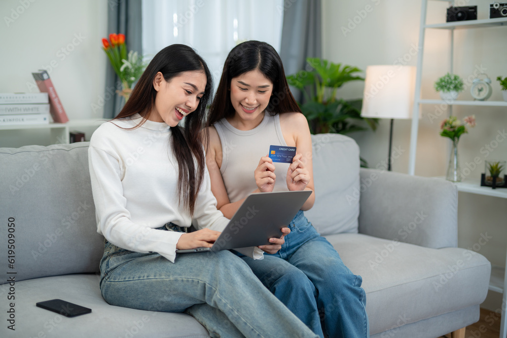 Two happy Asian young women use credit cards to make purchases. Shopping online with a laptop on the