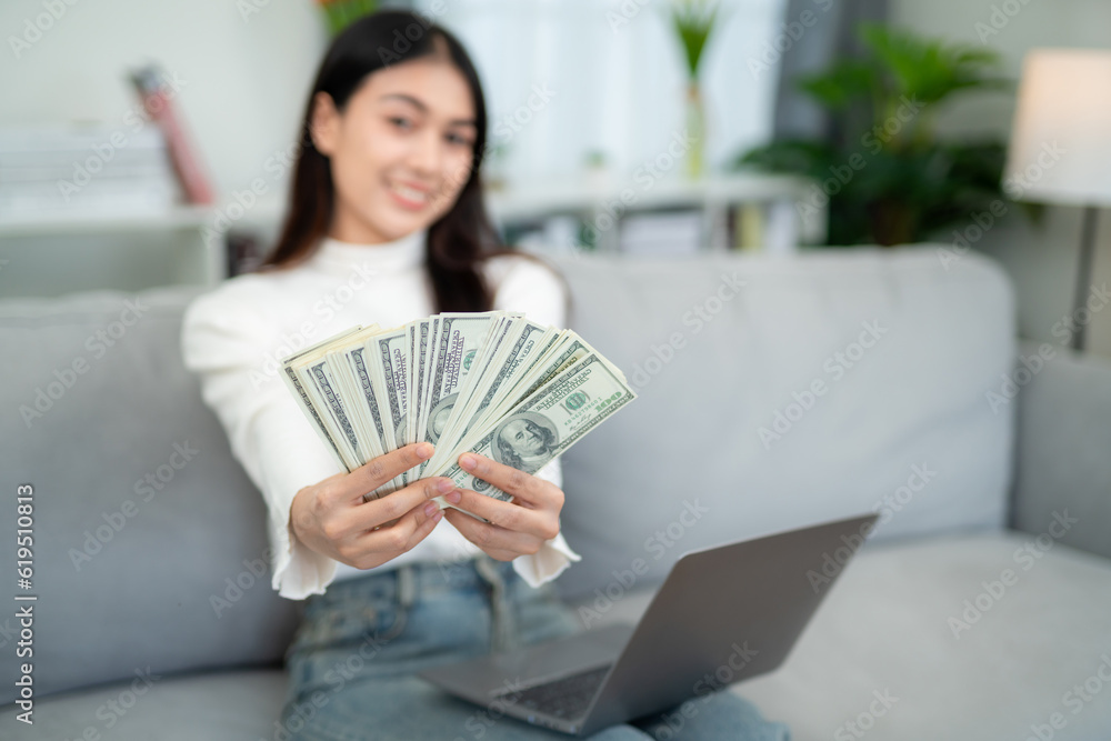 A woman showing cash with laptop on sofa in living room. online business and e-commerce concept.
