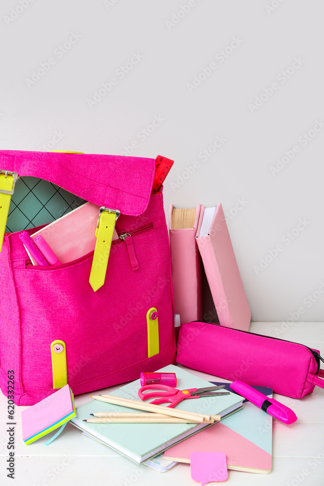 Pink school backpack with books, pencil case and stationery on white wooden table near wall