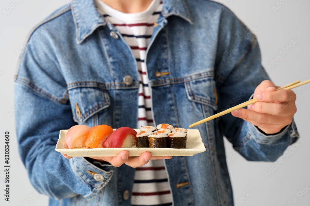 Young man with tasty sushi on light background, closeup