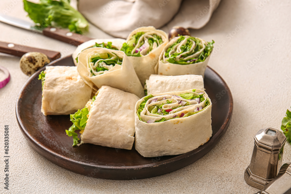 Plate of tasty lavash rolls with onion and greens on light background