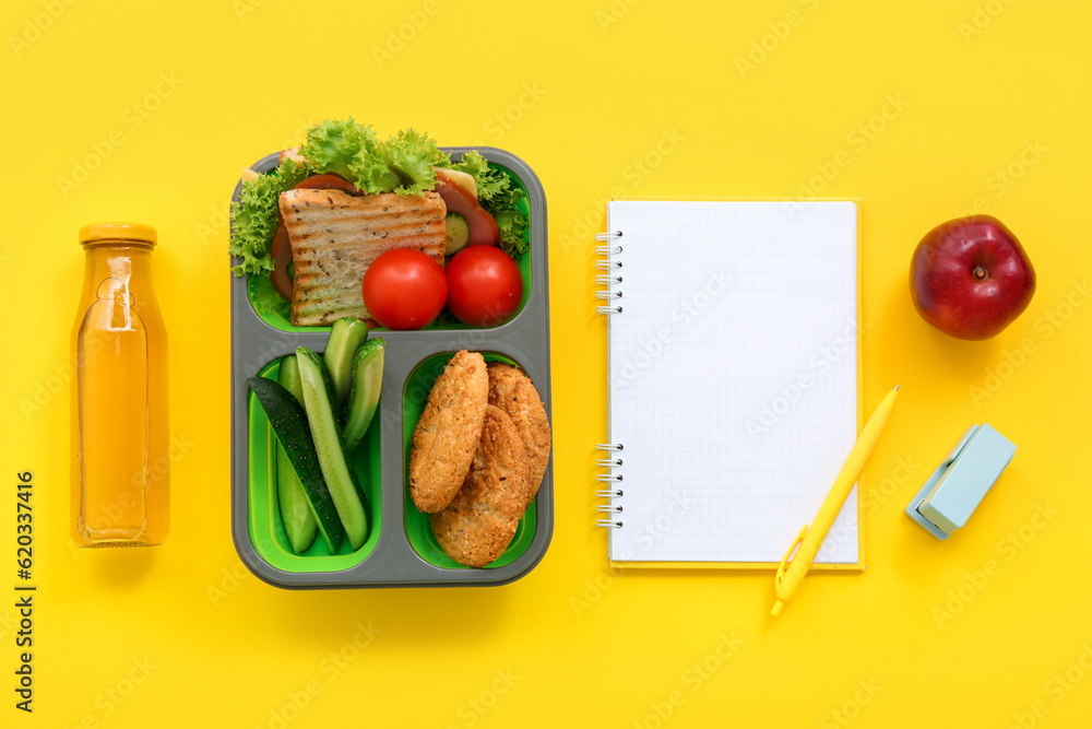 Stationery, blank notebook, drink and lunch box with tasty food on yellow background