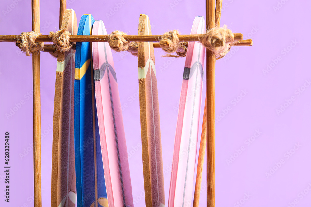 Stand with different mini surfboards on lilac background