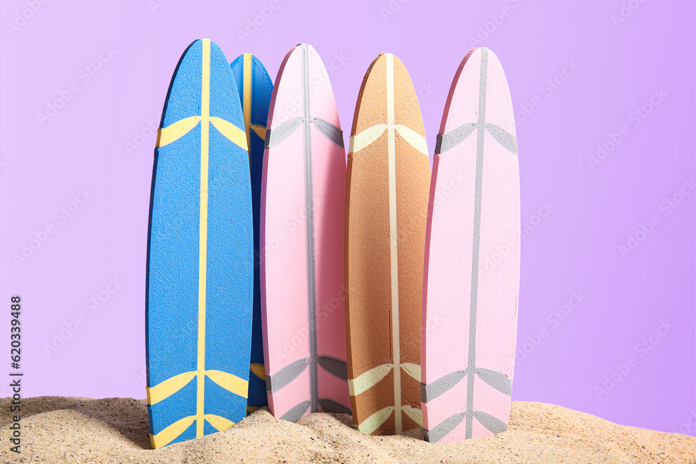 Different mini surfboards on sand against lilac background
