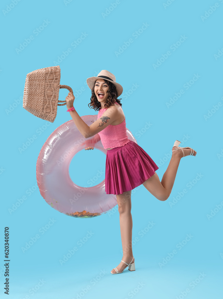 Young woman with beach bag and inflatable ring on blue background