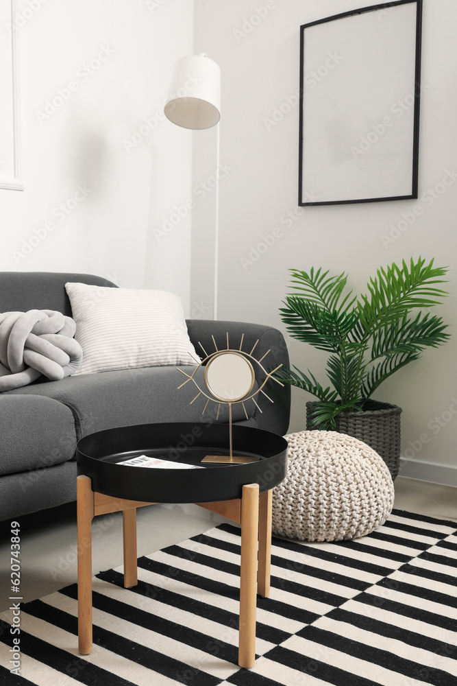 Interior of light living room with grey sofa and mirror on coffee table