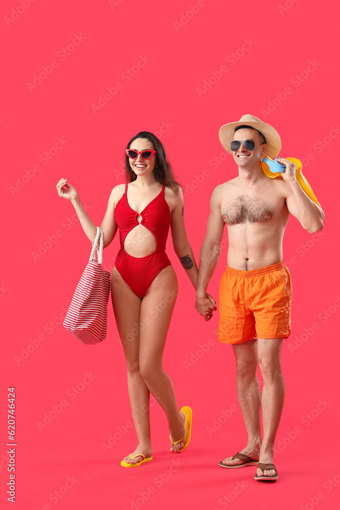 Young couple with beach bag and flippers holding hands on red background